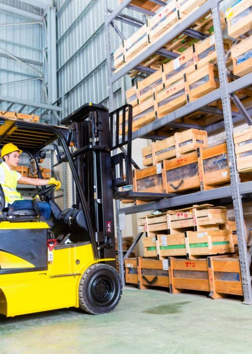 Asian fork lift truck driver lifting pallet in storage warehouse